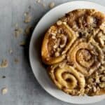Round plate of almond sticky buns on grey background with almonds sprinkled around