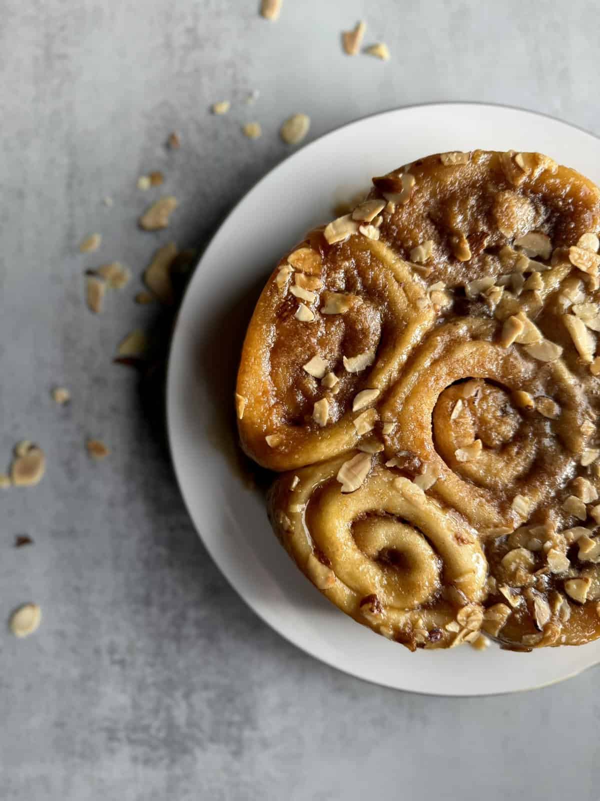 Round plate of almond sticky buns on grey background with almonds sprinkled around