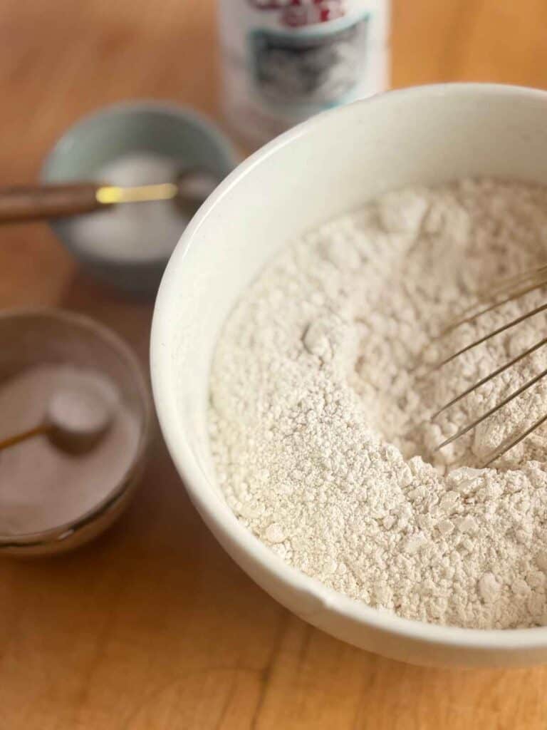 flour in bowl with whisk surrounded by baking powder and baking soda in smaller bowls