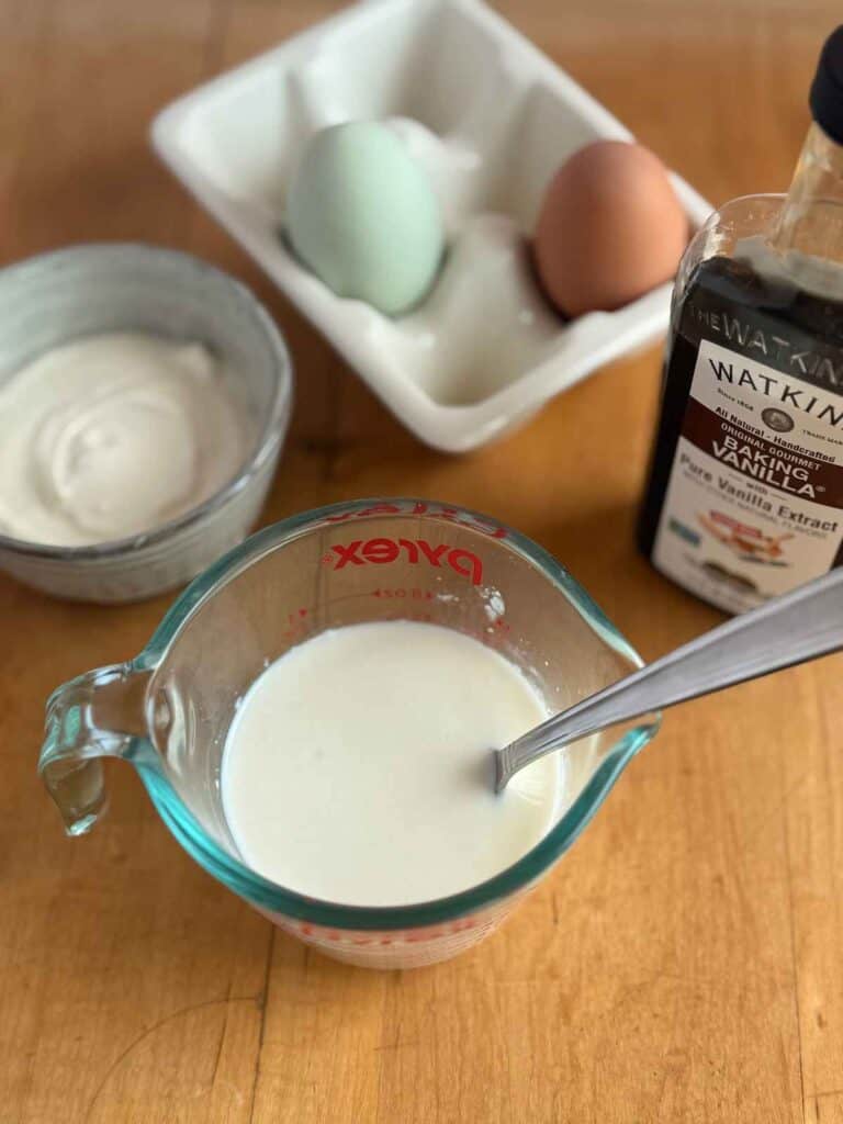 glass measuring cup with milk. sour cream in bowl, eggs, and vanilla extract 