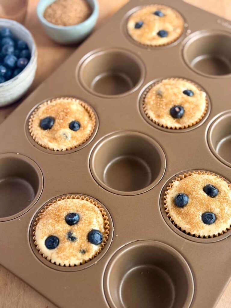 bakery-style blueberry muffins scooped in muffin tin sprinkled with turbinado sugar 