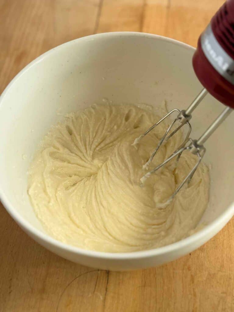 creamed butter and sugar being mixed with hand mixer in white bowl 