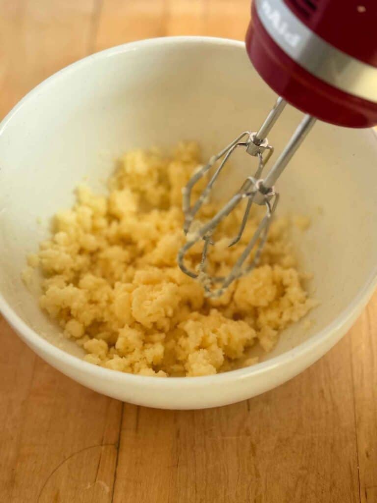 butter and sugar being mixed with hand mixer in white bowl 