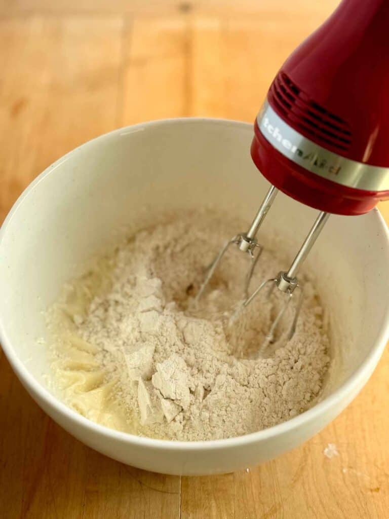 dry ingredients being mixed into creamed butter and sugar using a hand mixer