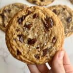brown butter sourdough chocolate chip cookie holding in hand close up with cookies in background