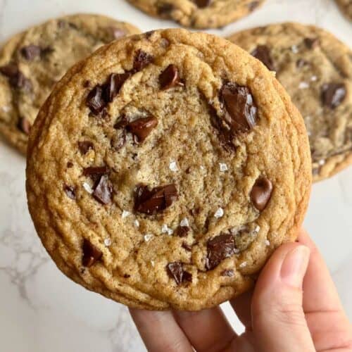 brown-butter-sourdough-chocolate-chip-cookie-holding-in-hand-close-up-with-cookies-in-background