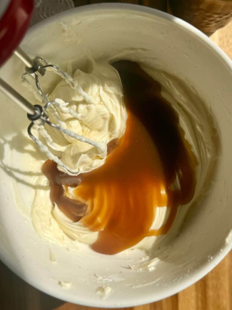 brown butter pumpkin cake-butterscotch cream cheese frosting in bowl with butterscotch added and mixer in corner
