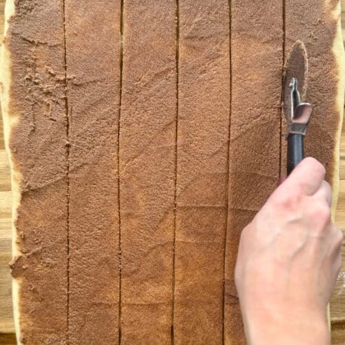 cast iron skillet cinnamon roll dough rolled out with filling cutting strips