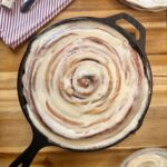 cast iron skillet cinnamon roll on wooden board red striped napkin and plates in corner