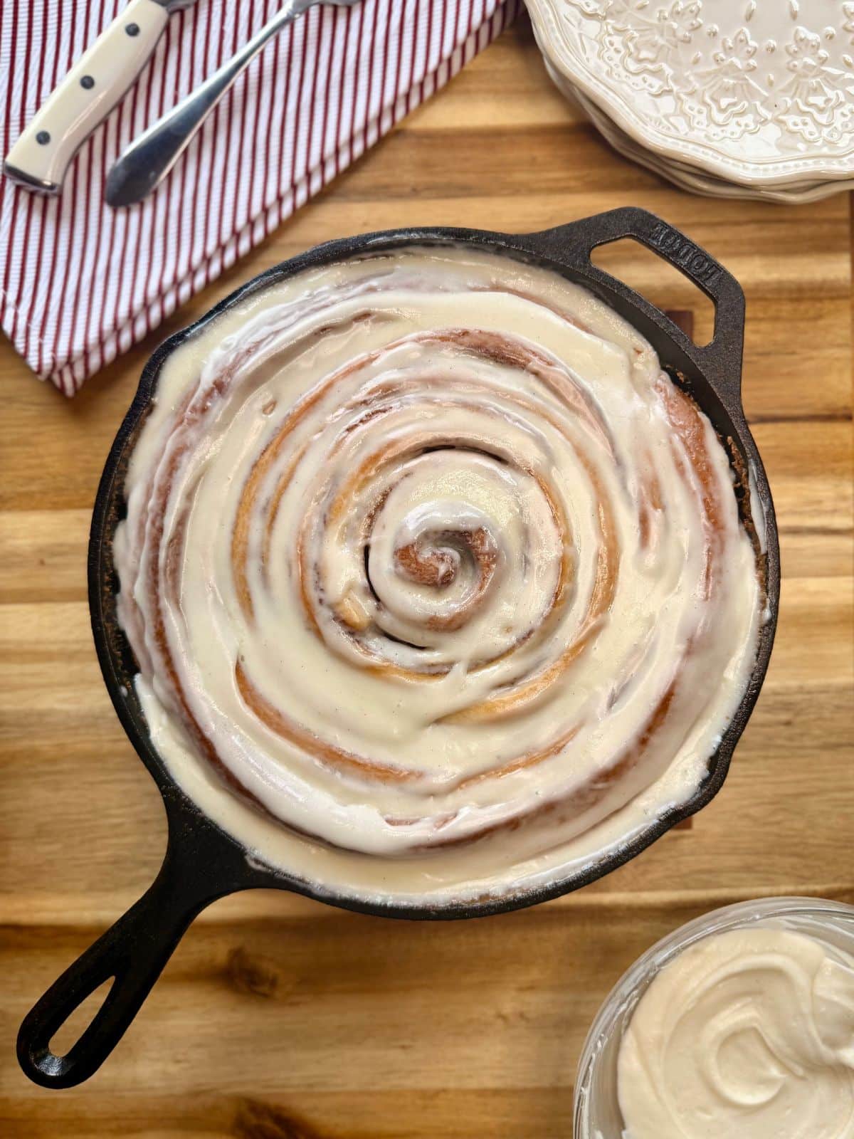 cast iron skillet cinnamon roll on wooden board red striped napkin and plates in corner