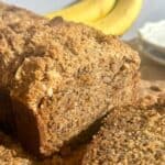 brown butter banana bread loaf with slice cut and bananas in background