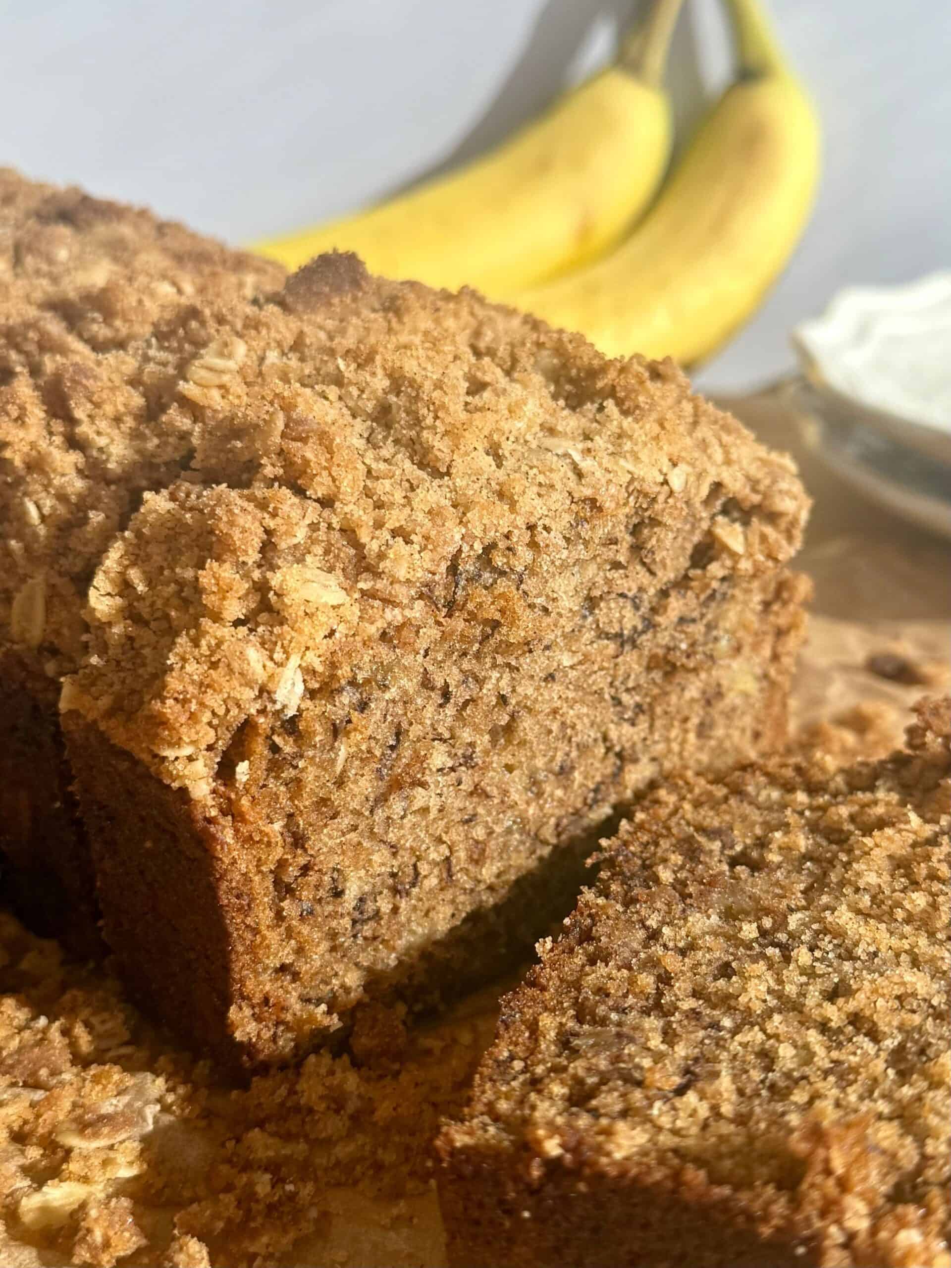 brown butter banana bread loaf with slice cut and bananas in background