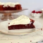 flourless red velvet torte slice on plate with torte on cake stand behind