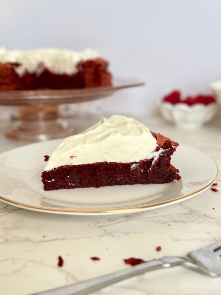 flourless red velvet torte slice on plate with torte on cake stand behind