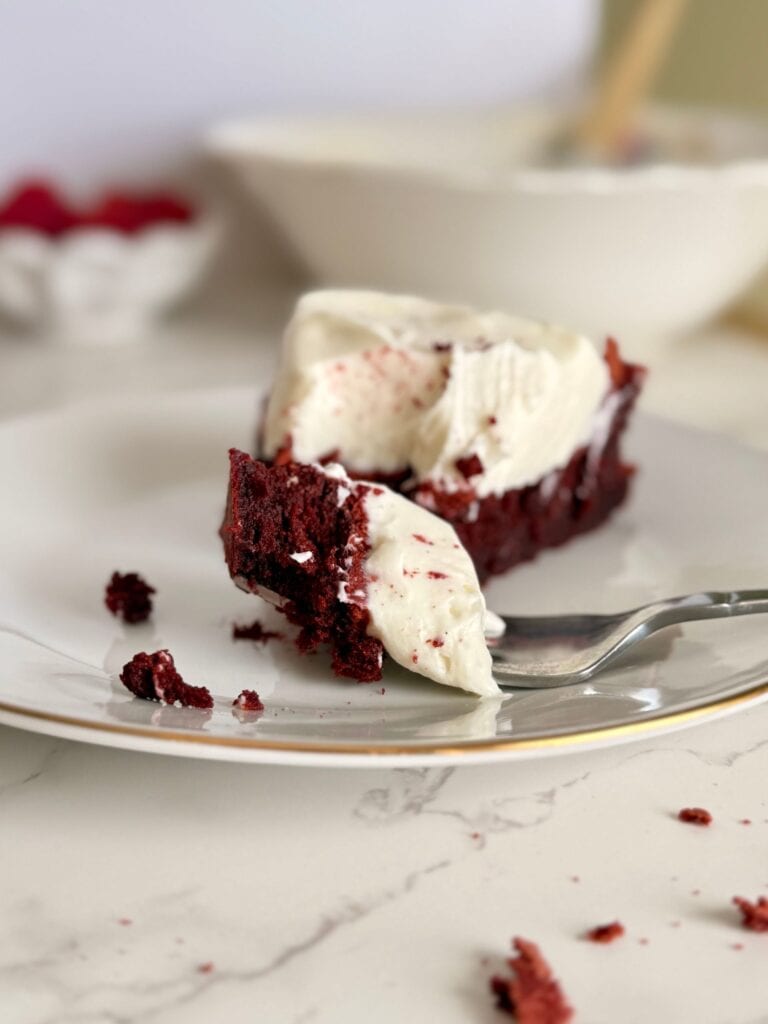 flourless red velvet torte slice on white plate with bit on fork with crumbs surrounding