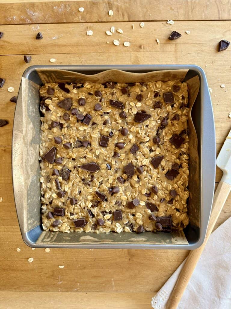 oatmeal chocolate chip cookie bars batter in square pan with chocolate chips on top before baking 