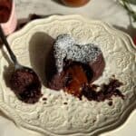 salted caramel molten lava cake on white plate with caramel molten center melting out and spoon with bite on it