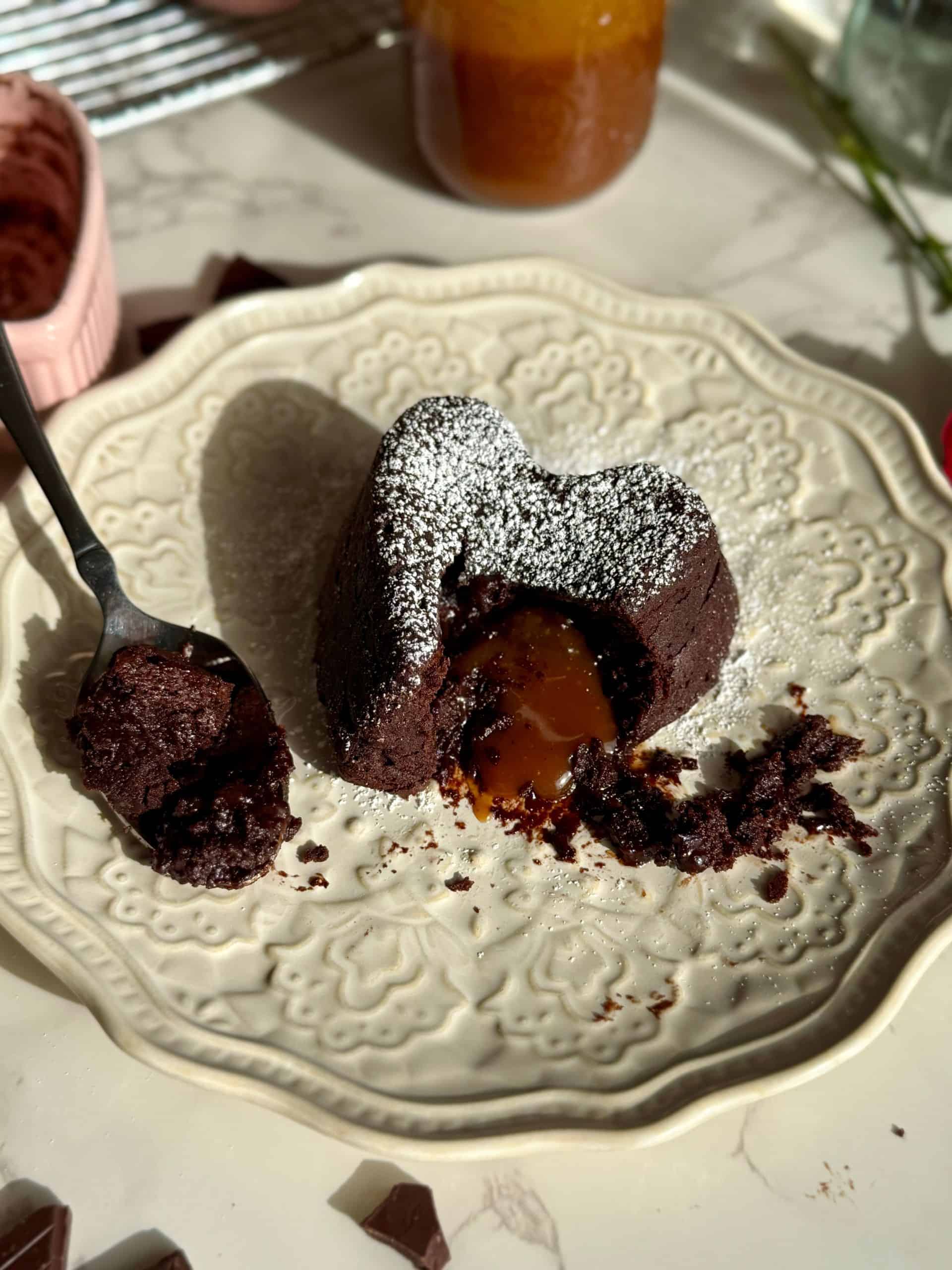 salted caramel molten lava cake on white plate with caramel molten center melting out and spoon with bite on it