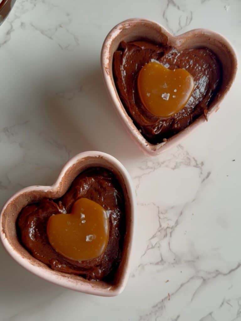 salted caramel molten lava cakes batter in two heart ramekins with caramel placed in center of each