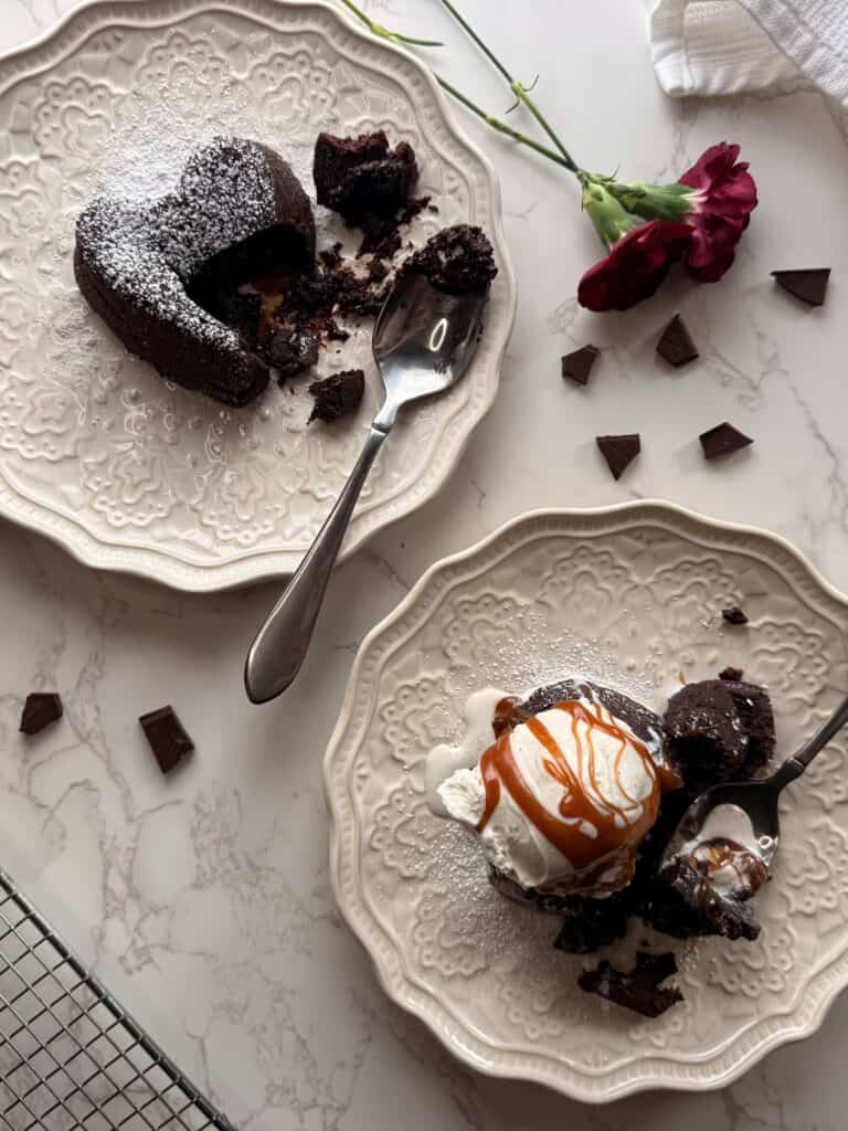 salted caramel molten lava cakes on plates one with bite taken out one with ice cream and caramel drizzled 