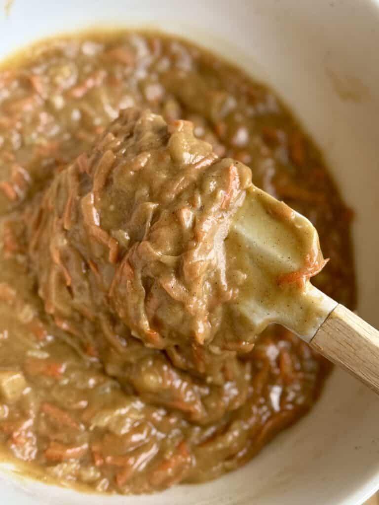 close up of carrot cake batter on spatula showing the the shredded carrots and pineapple pieces in the spiced batter
