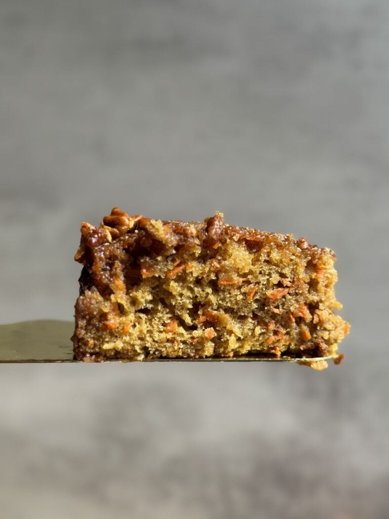 close up of carrot cake on serving spatula showing the moist texture of the cake with shreds of carrots and caramelized pecans on top