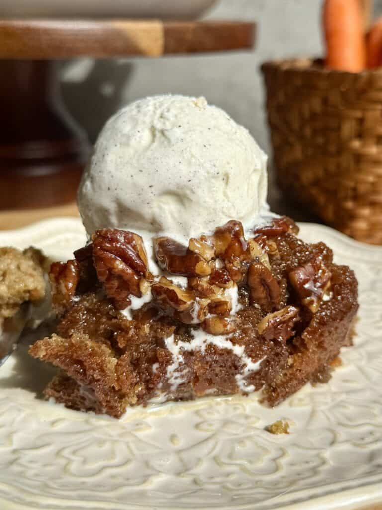 sticky pecan carrot cake slice on plate with scoop of vanilla ice cream melting over top the caramelized pecans 
