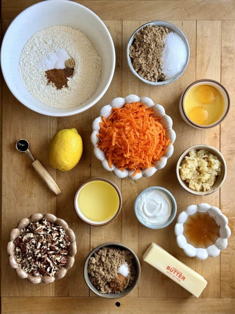 ingredients for sticky pecan carrot cake arranged on wooden board including carrots, pineapple, pecans, butter, brown sugar, and more