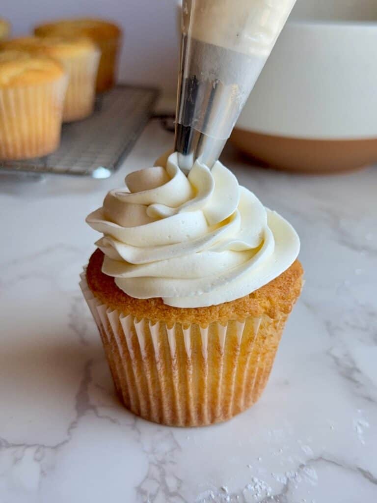 piping buttercream swirl on top of vanilla cupcake