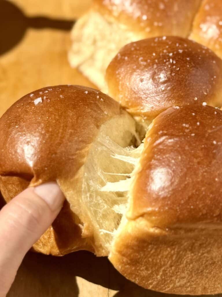 Pulling apart a soft and fluffy dinner roll to reveal the light, feathery layers inside.