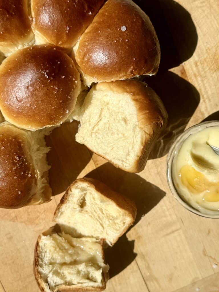 Overhead view of soft and fluffy dinner rolls with a few pulled apart to show the feathery interior, served with salted honey butter.
