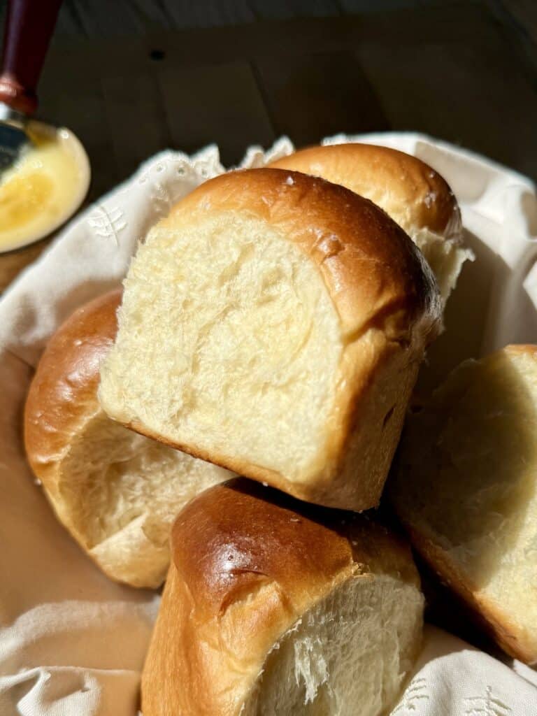 Soft and fluffy dinner rolls with golden brown tops, torn apart and stacked in basket to show the light, feathery interior crumb.