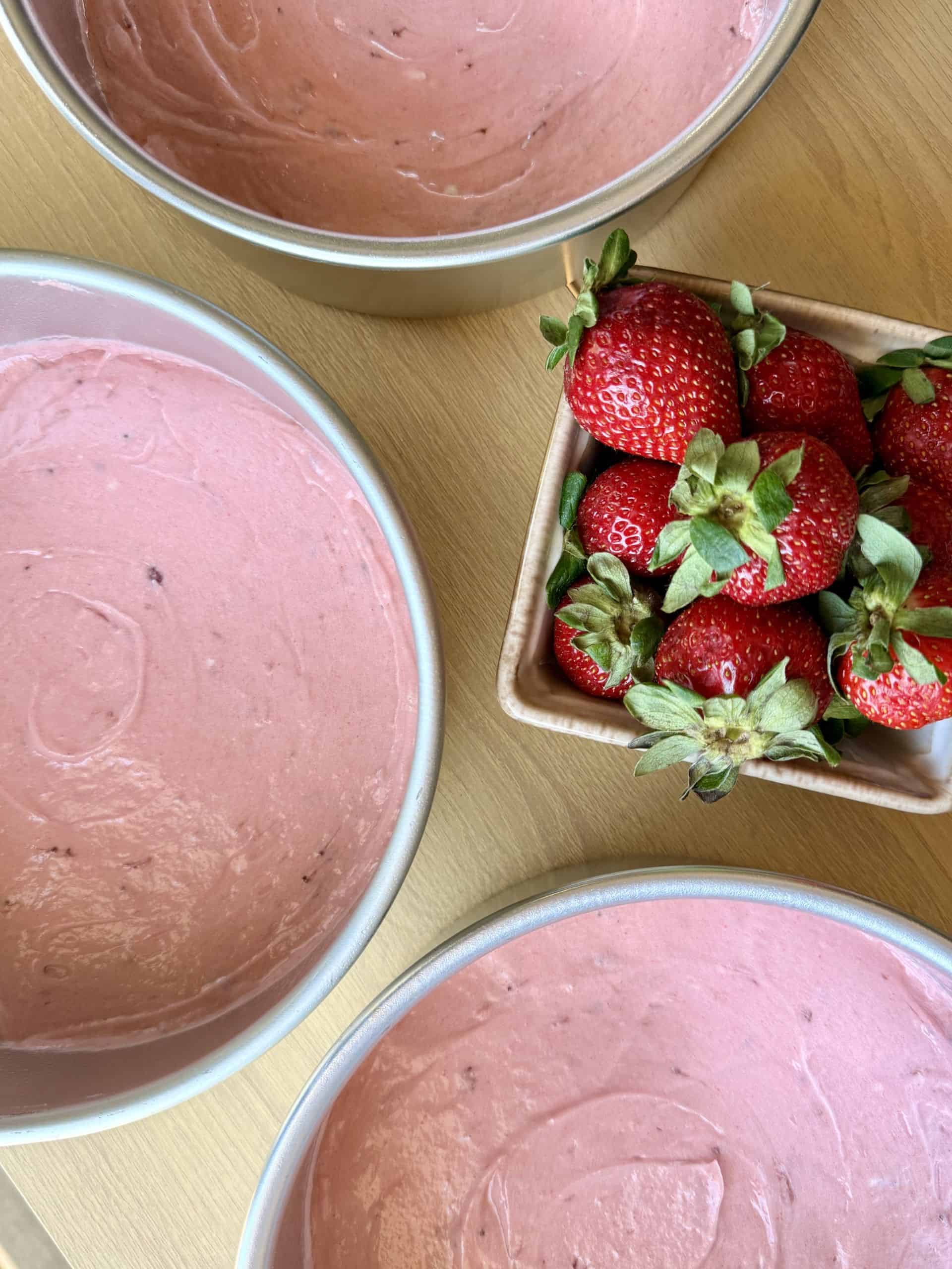 Strawberry cake batter prepared in three round cake pans with fresh strawberries