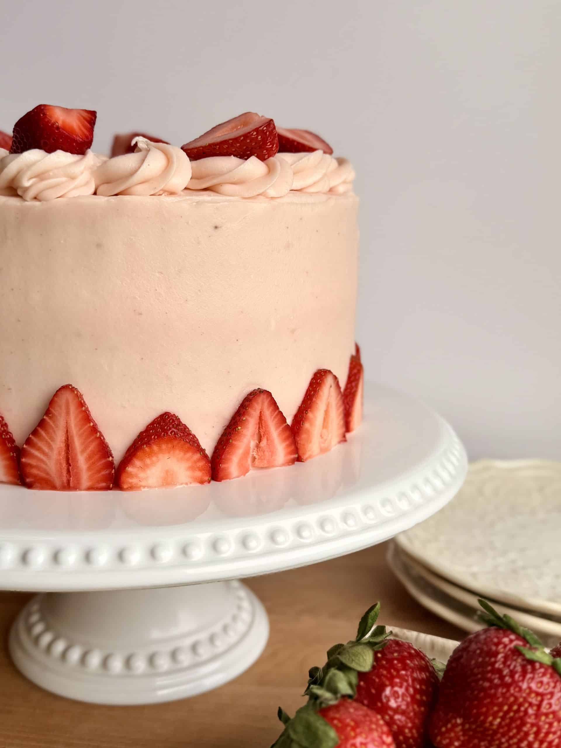 Strawberry cake with strawberry cream cheese frosting displayed on a cake stand decorated with fresh sliced strawberries