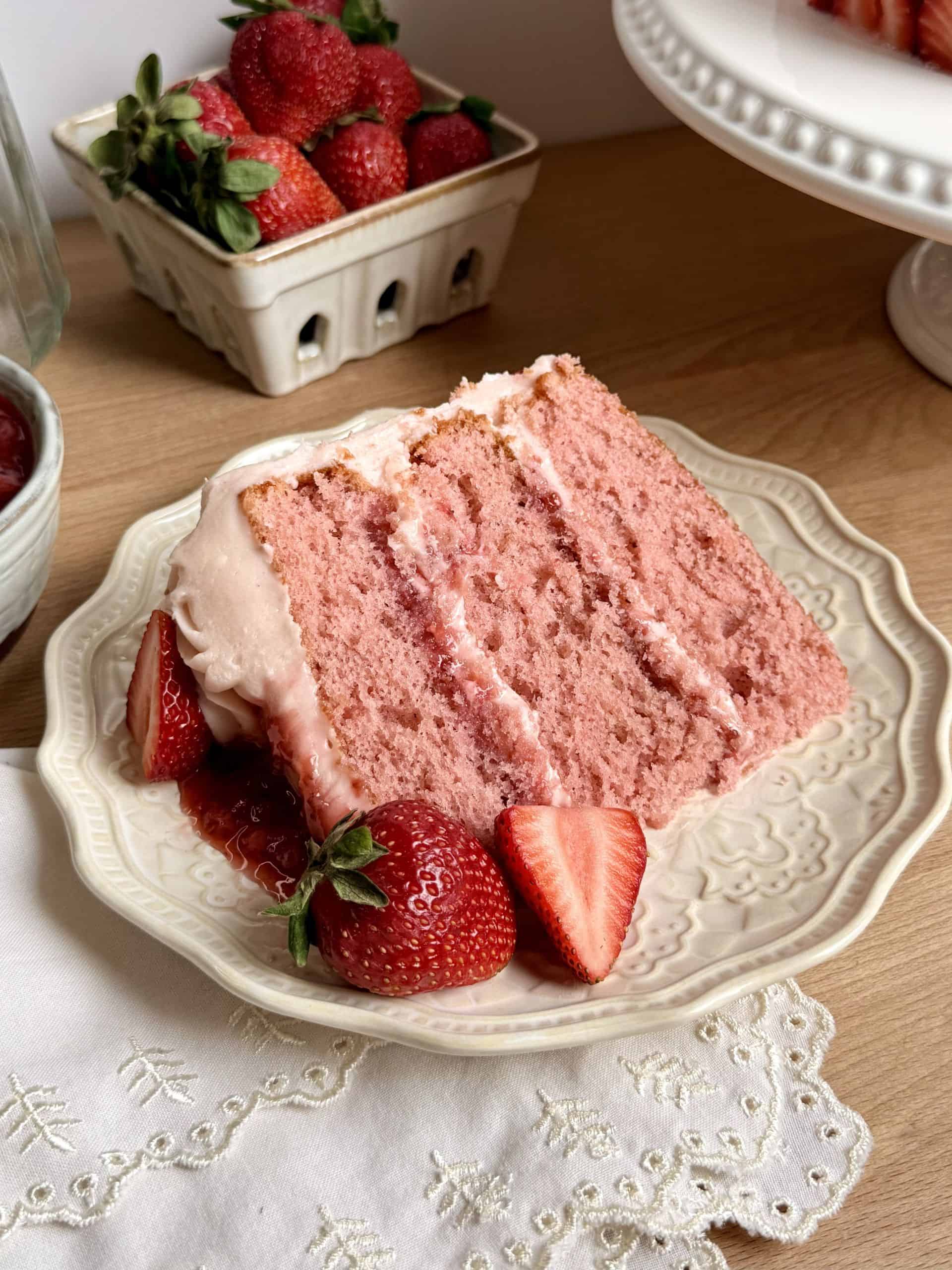 Slice of strawberry cake with homemade strawberry jam filling and cream cheese frosting on a plate