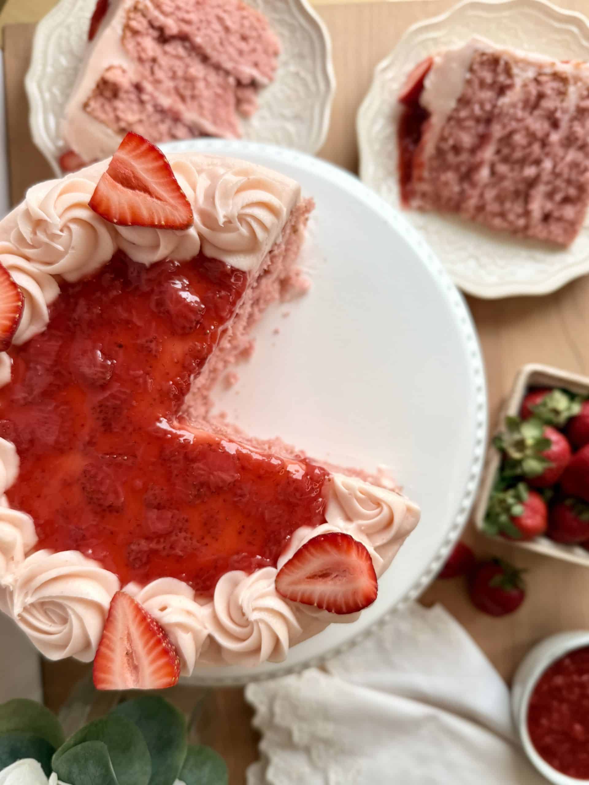 Strawberry cake with slices cut out showing strawberry jam filling, soft fluffy strawberry cake, and cream cheese frosting