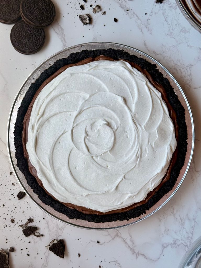 third and final layer of the triple layer Oreo cream pie, light and fluffy whipped cream decoratively swirled on top 