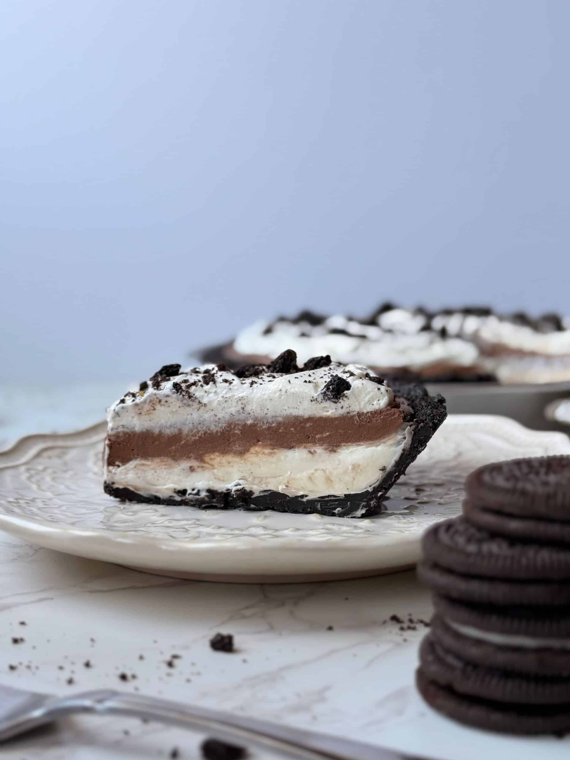 slice of triple layer Oreo cream pie on a plate showing all the creamy layers and Oreo crust