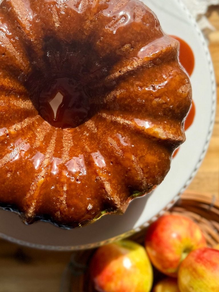 apple bundt cake on cake stand drizzled with gooey salted caramel and honeycrisp apples to the side