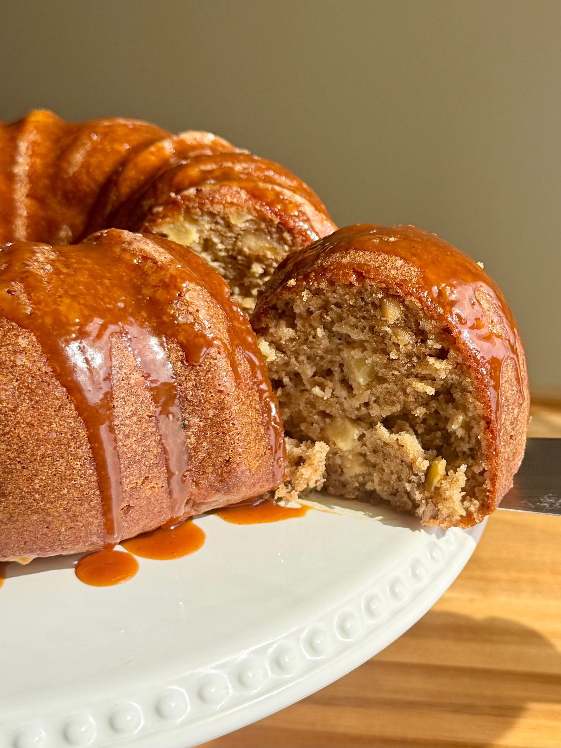 salted caramel apple bundt cake with slice cut out showing tender crumb and apple chunks with caramel drizzled on top
